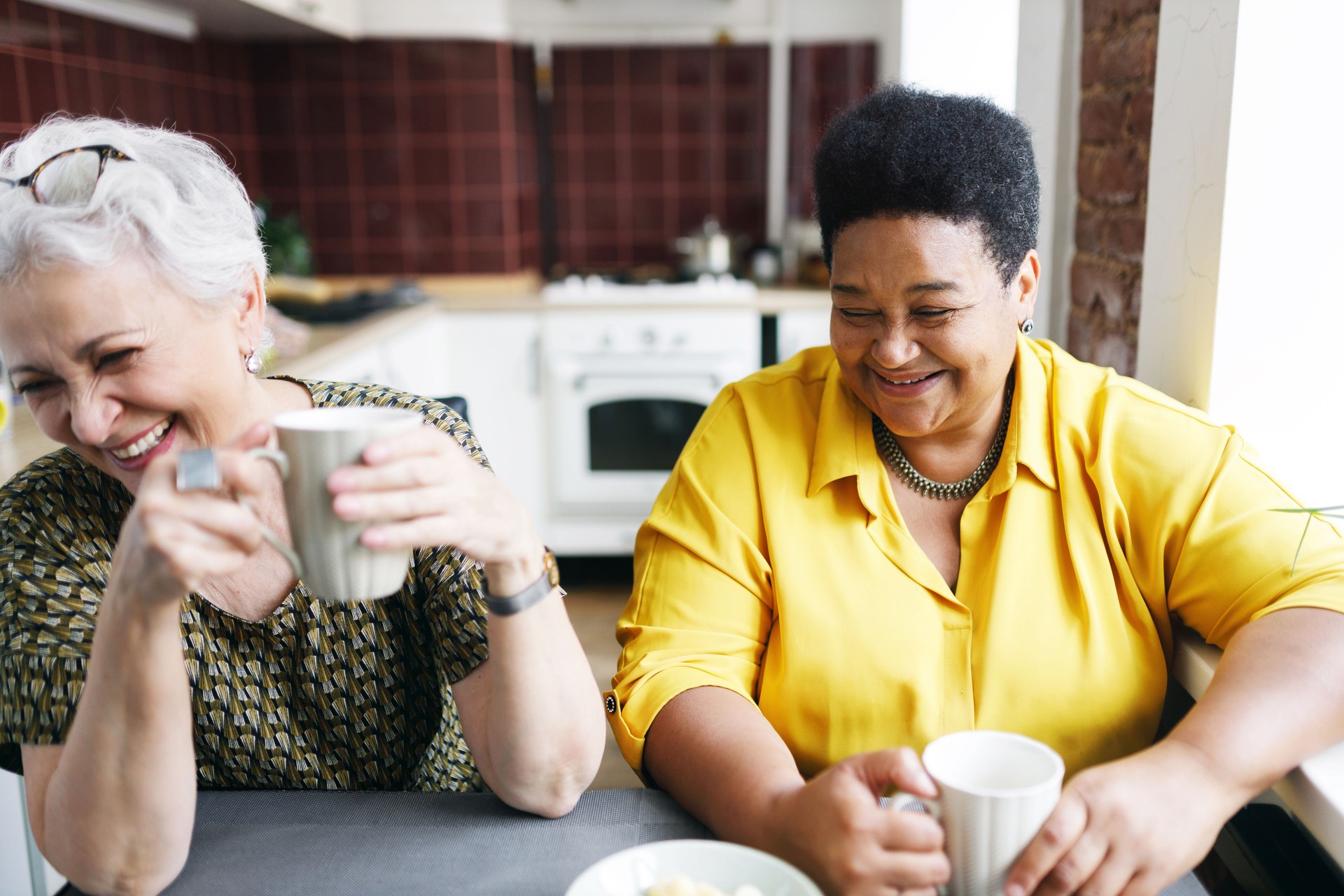 Friendship for life. Retired female friends of diverse ethnicity drinking coffee together after long time no seeing each other, laughing out loud at joke or situation, sharing stories and news